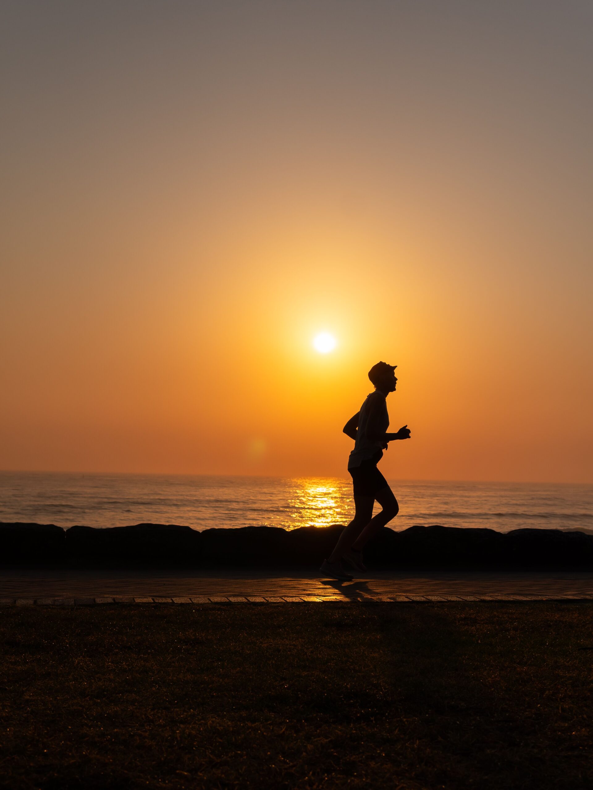 A silhouette of a person running along the ocean shore during a picturesque sunset.